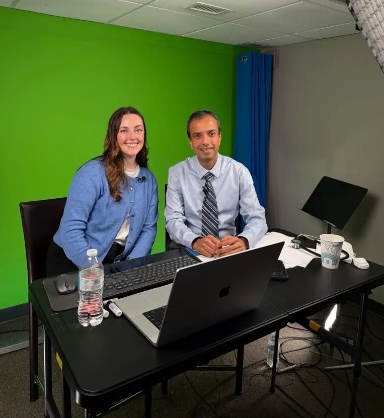 Two people sitting at a table in front of a greenscreen